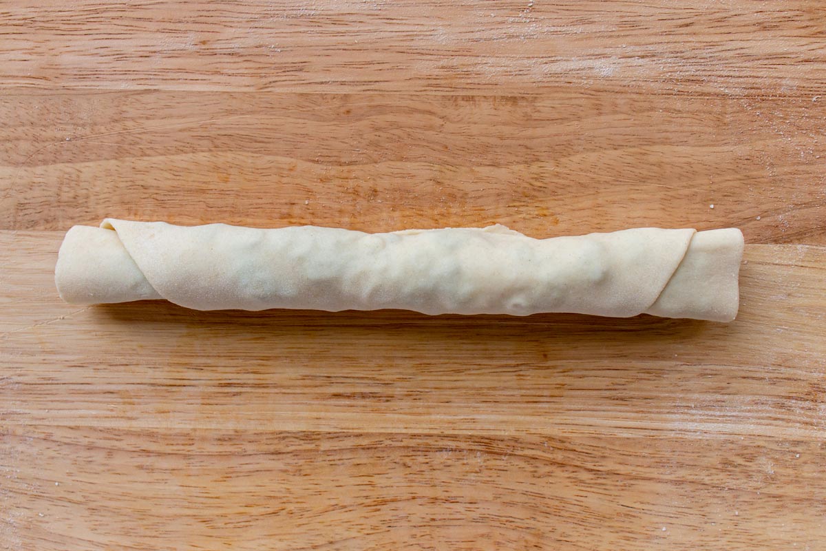 Dough rolled into a long snake shape on a wooden board.
