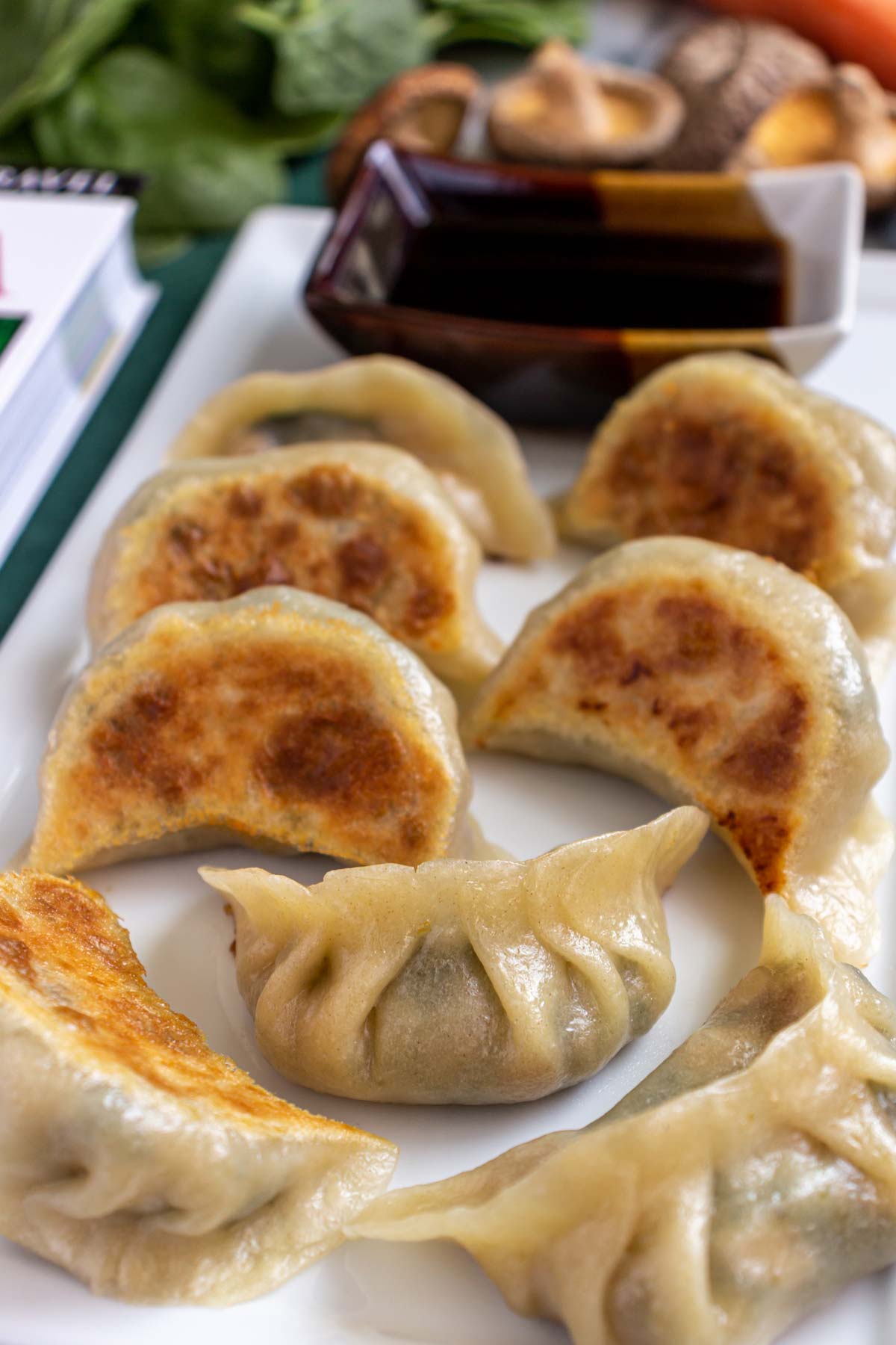 Crispy vegetable potstickers with dipping sauce on a white rectangular plate.