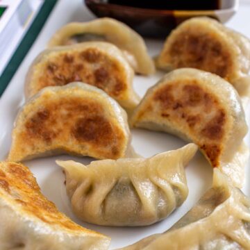 Crispy vegetable potstickers with dipping sauce on a white rectangular plate.