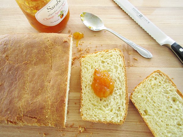 overhead view of a partially sliced loaf of brioche with orange jam on one slice