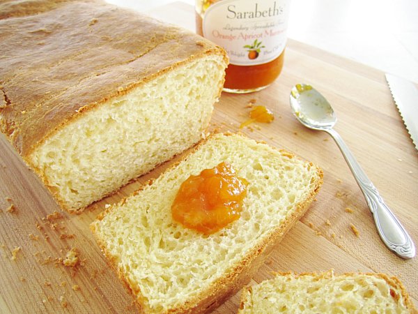 a partially sliced loaf of brioche with a dollop of orange marmalade on one slice