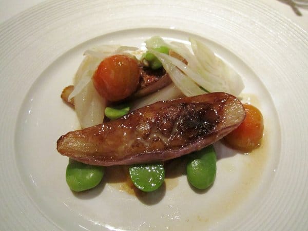 a small grilled eggplant served with fava beans and small tomatoes on a white plate