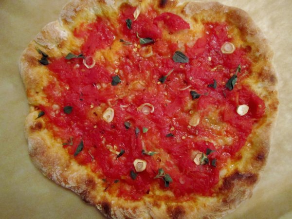 A closeup of a pizza with red tomato sauce, sliced garlic, and fresh herbs