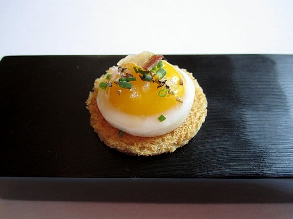 closeup of a small round toast topped with an egg and chives on a black surface