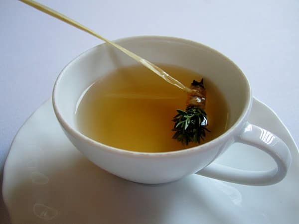 a white teacup filled with light brown liquid and a small bundle of herbs