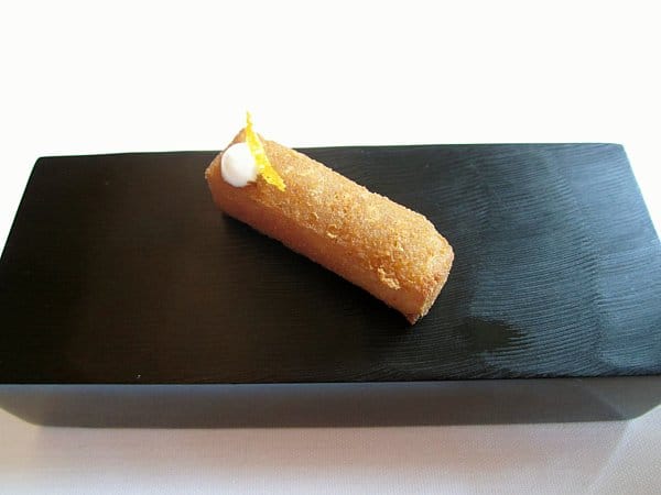 closeup of a small rectangular fried food item topped with lemon zest on a black surface