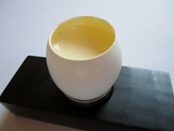 an egg shell filled with a creamy liquid served on a black dish