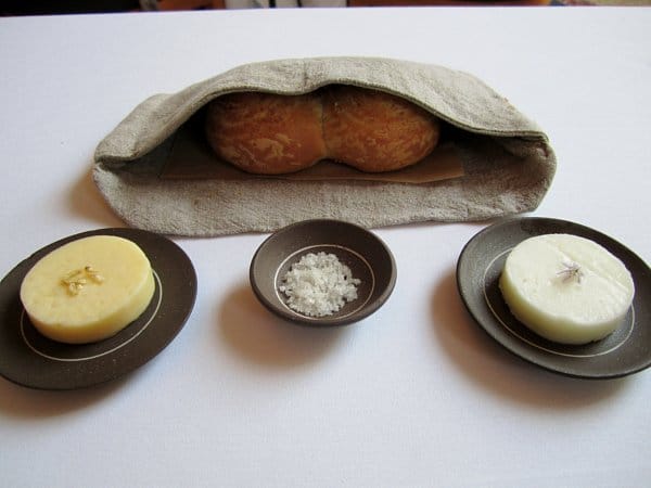 a fabric pocket filled with bread rolls, circular pats of butter, and a dish of salt