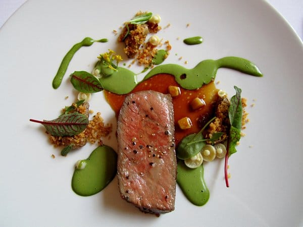 overhead view of a slice of steak surrounded by tiny mushrooms and green sauce drizzle