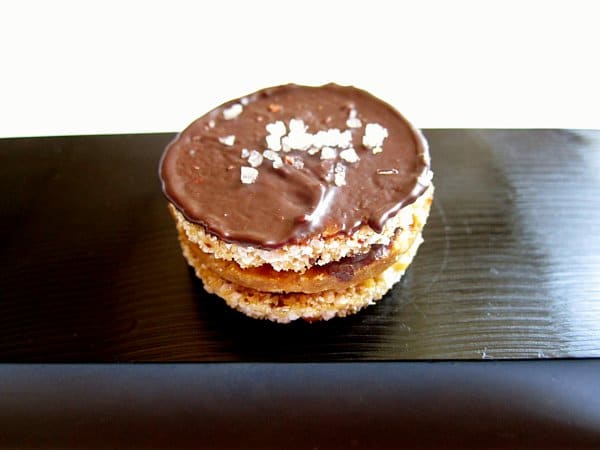 a sandwich cookie topped with chocolate and salt flakes on a black surface