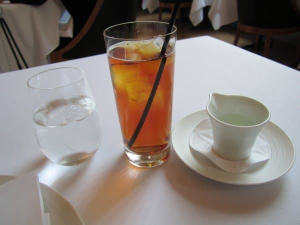 a tall glass of iced tea next to a glass of water on a white table