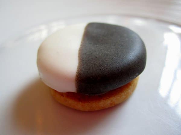 a small cookie with half white and half black frosting on top on a white plate