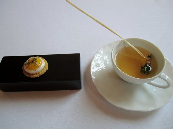 a small round toast topped with a quail egg next to a cup of tea
