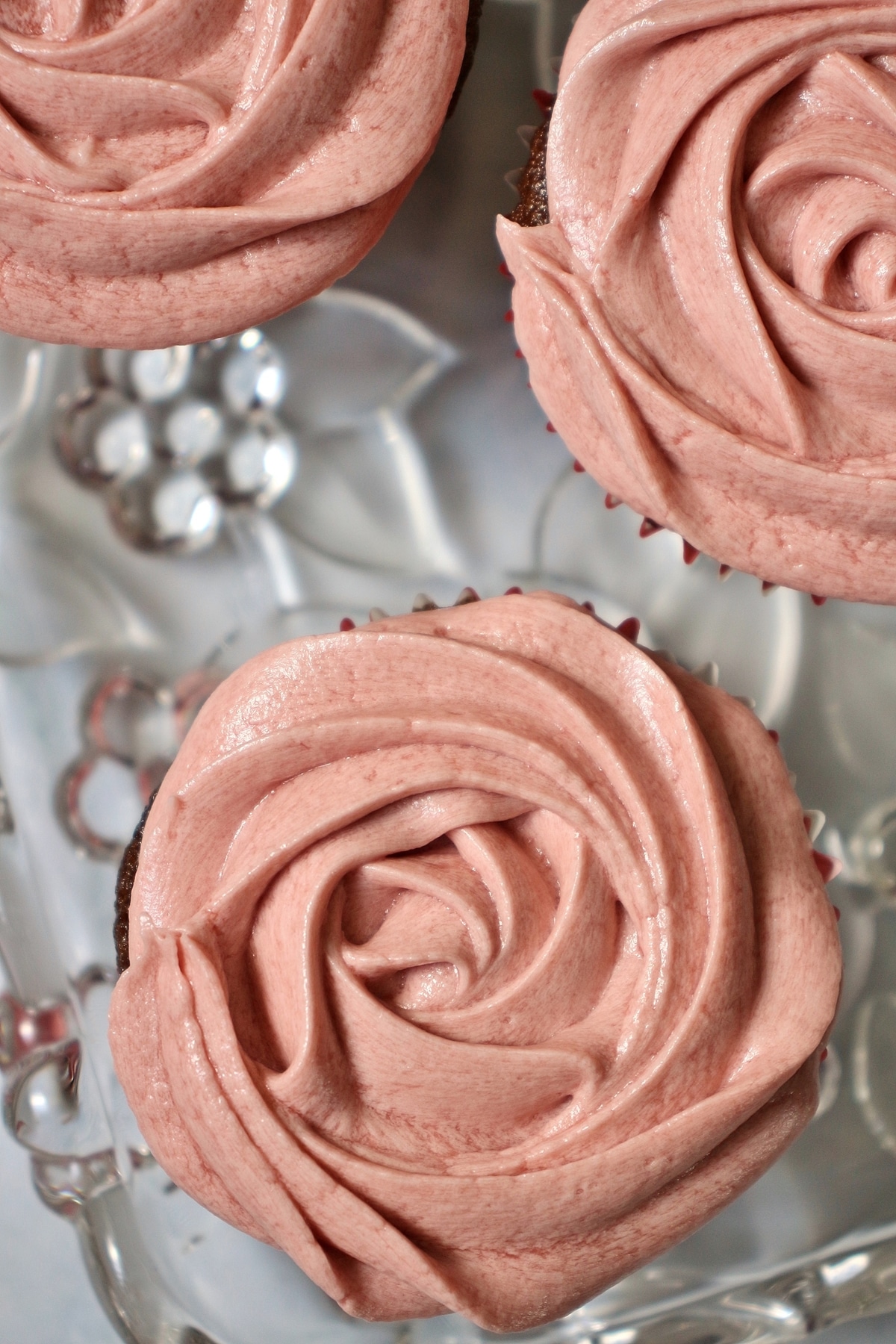 overhead view of 3 cupcakes with pink frosting that looks like a rose