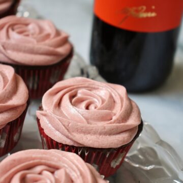 chocolate cupcakes with red wine frosting on a glass tray, with a bottle of red wine