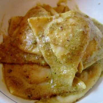 closeup of a bowl of triangular tortelli in green pistachio pesto