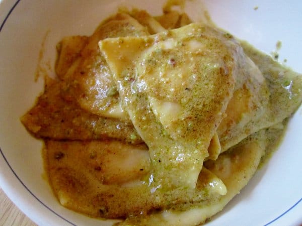 closeup of a bowl of triangular tortelli in green pistachio pesto