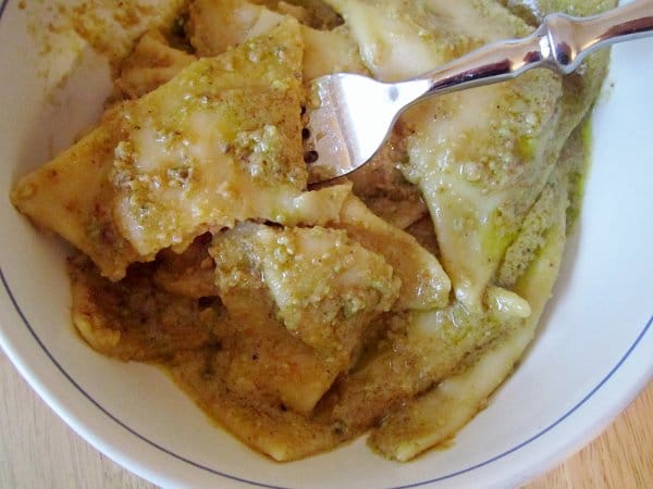 overhead view of a bowl of half-eaten triangular tortelli in green pistachio pesto