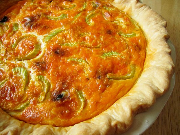 A closeup of a buffalo chicken quiche with buffalo sauce and sliced celery on top.