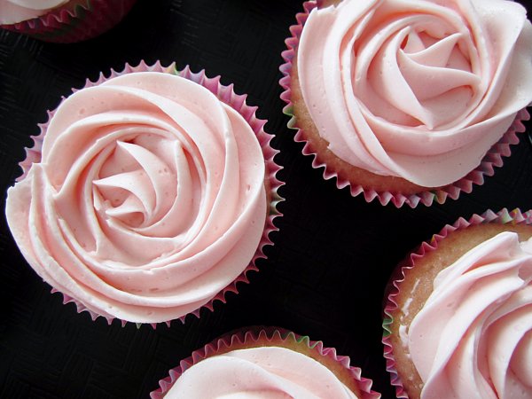 overhead closeup of cupcakes on a black surface with pink frosting that resembles a rose