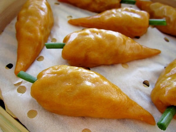 closeup side view of carrot shaped dumplings in a bamboo steamer basket