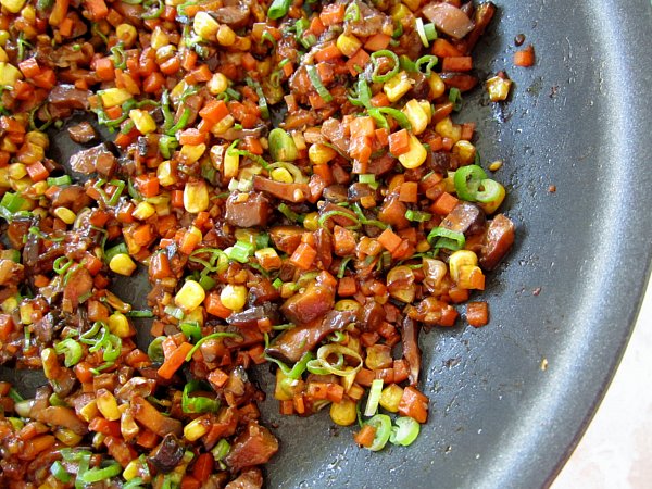 A pan filled with cooked chopped carrots, mushrooms, corn, and scallions