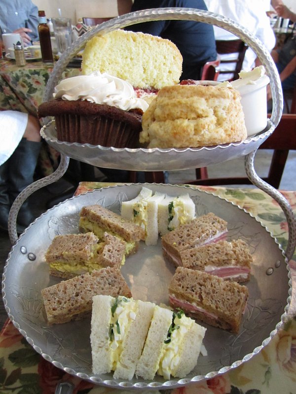 a metal two tiered display of tea sandwiches, scones and sweets