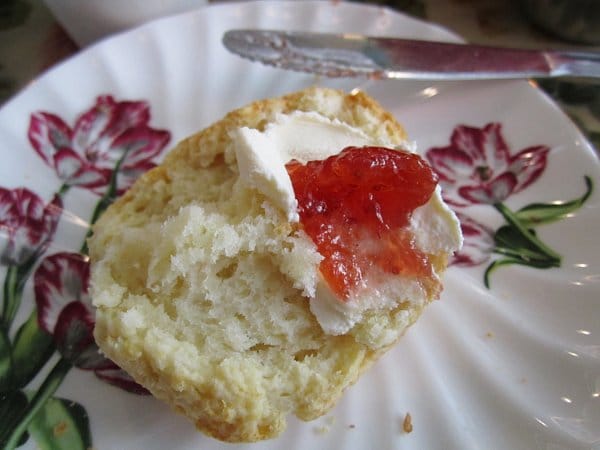 a closeup of a halved scone topped with clotted cream and strawberry jam