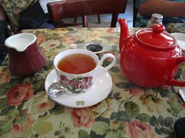 A table topped with a cup of tea and a red ceramic tea pot