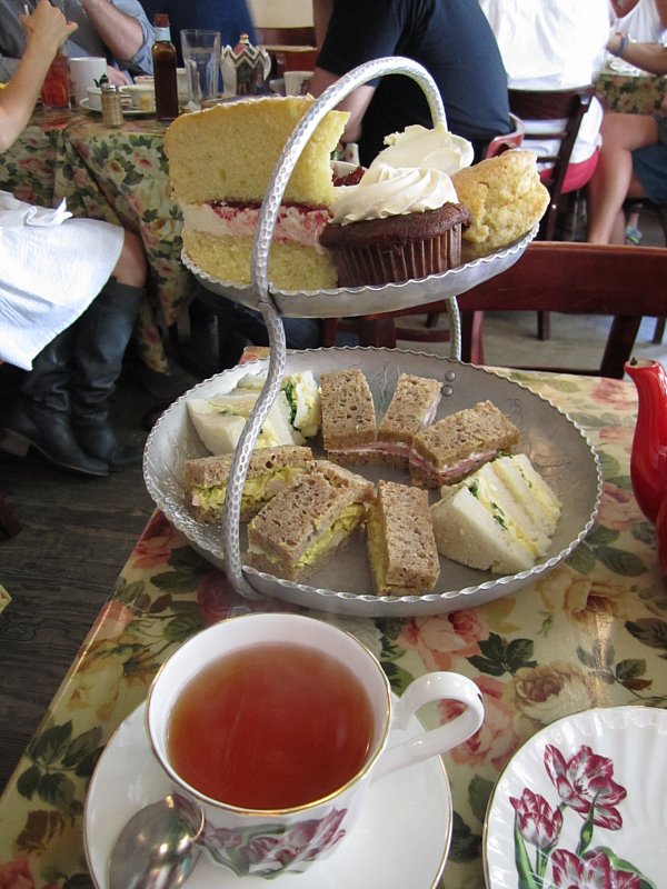 a cup of tea in front of a two-tiered afternoon tea display of sandwiches and sweets