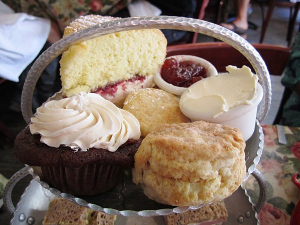 a closeup of scones, cakes, jam and clotted cream on a metal surface