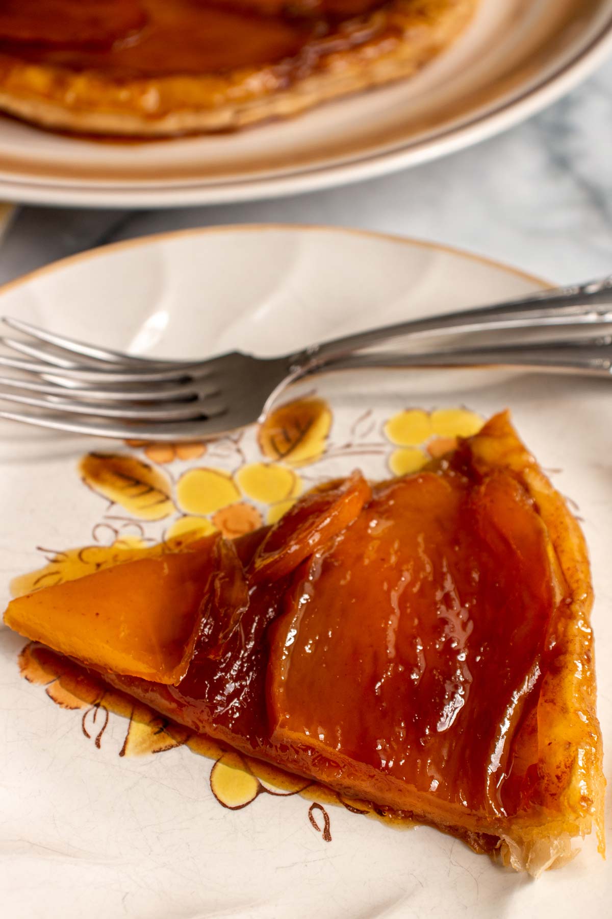 Closeup of a slice of mango tarte tatin on a rustic plate with two forks.