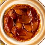 A caramelized layer of sliced mangos on a round tart served on a platter.