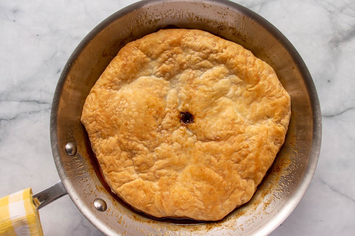 A golden brown baked disc of puff pastry in a metal frying pan.