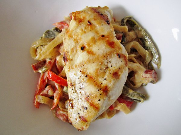 overhead view of a grilled chicken breast over cooked peppers and onions in a white dish