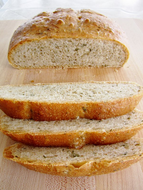 a partially sliced loaf of fresh thyme bread on a wooden board