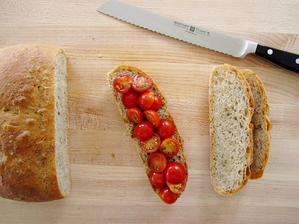 overhead view of sliced bread topped with halved cherry tomatoes on a wooden board