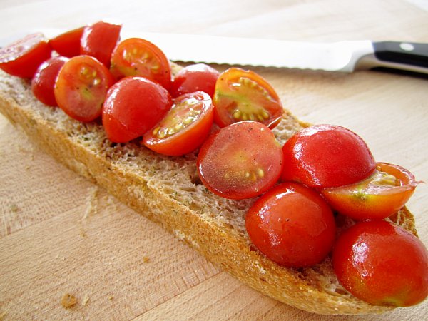 a closeup of a slice of bread topped with red cherry tomatoes on a wooden board