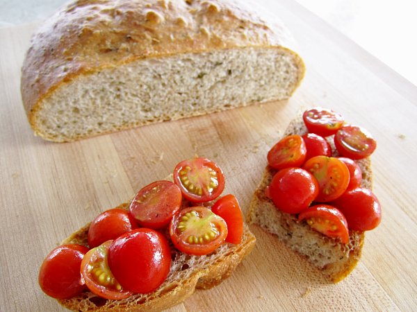 two pieces of bread topped with cherry tomatoes on a wooden board