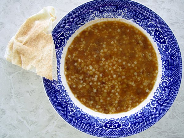 a blue and white shallow bowl of lentil soup with a piece of pita bread