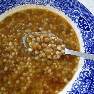 closeup of a bowl of lentil soup with macaroni with a spoon scooping some out
