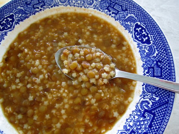 closeup of a bowl of lentil soup with macaroni with a spoon scooping some out