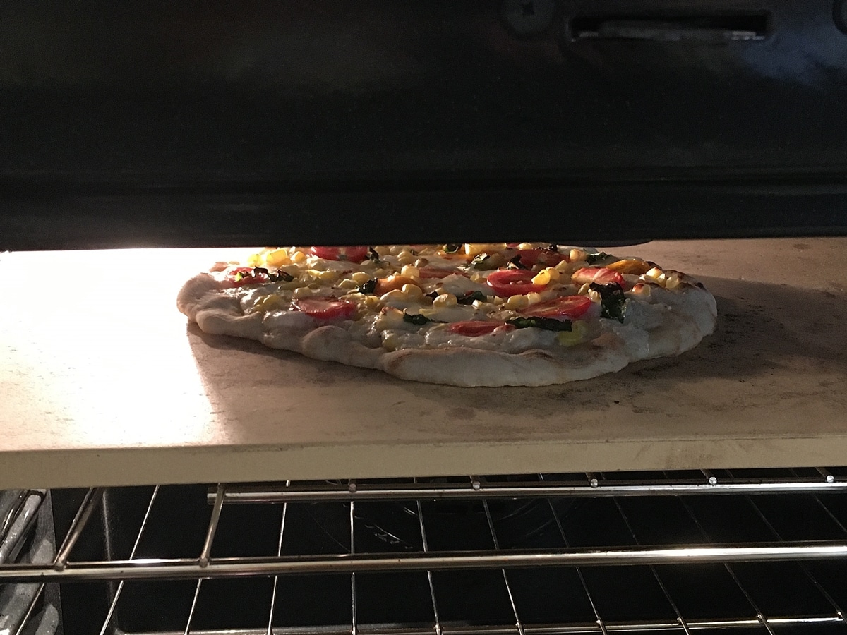 a pizza on a pizza stone in the oven under a broiler