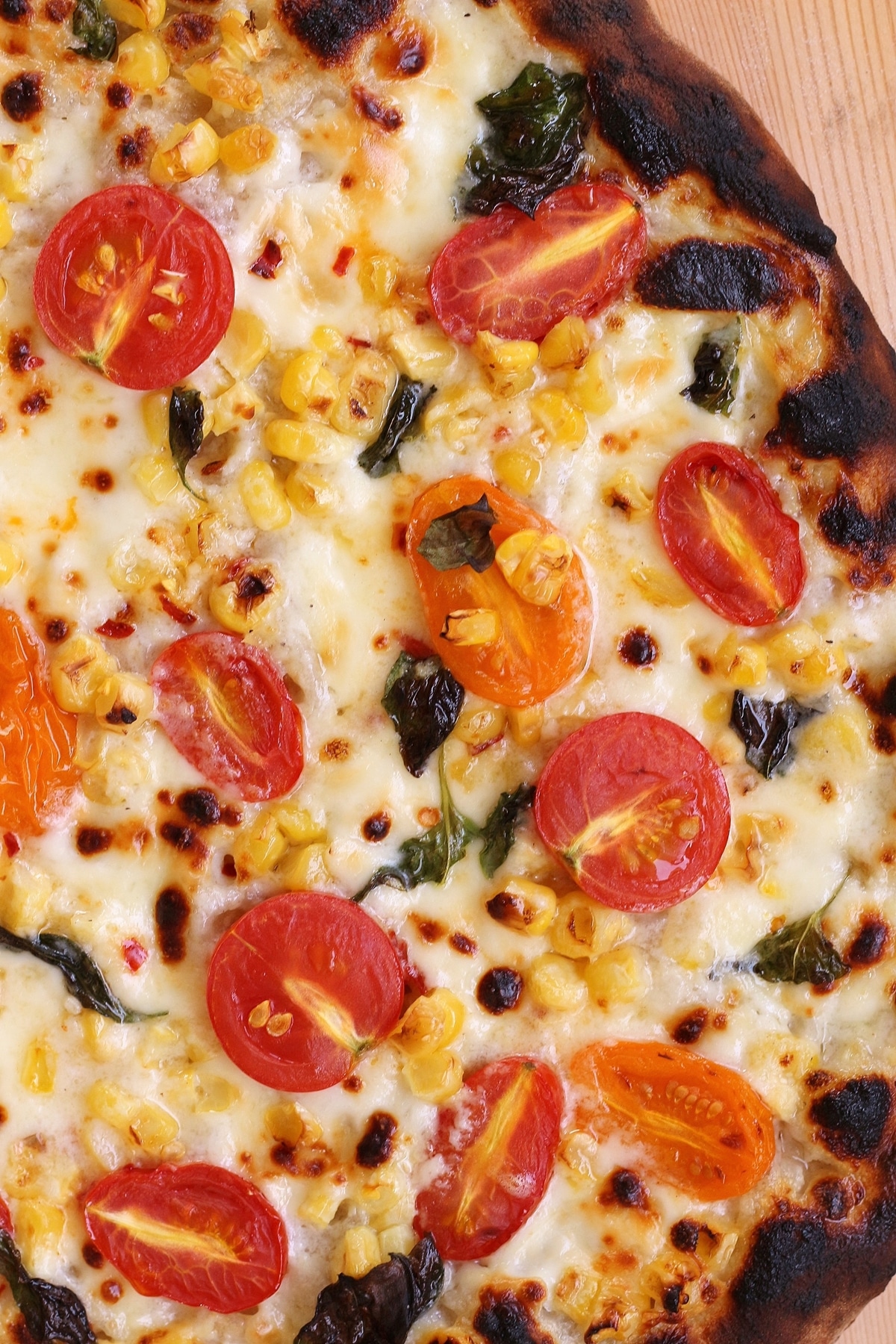 overhead closeup of a bubbly white pizza topped with corn and cherry tomatoes