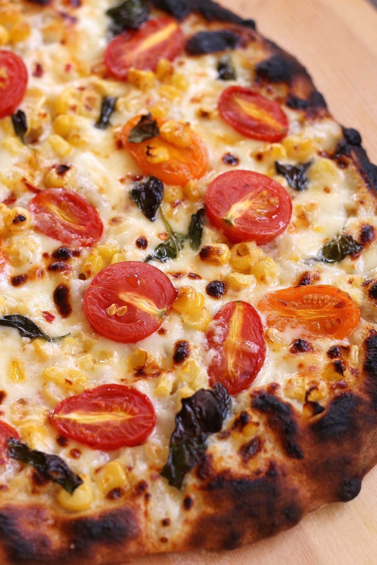 a closeup of a charred pizza topped with fresh corn and halved cherry tomatoes