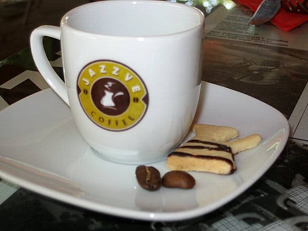 A coffee cup on a table with a small cookie and coffee beans on the side