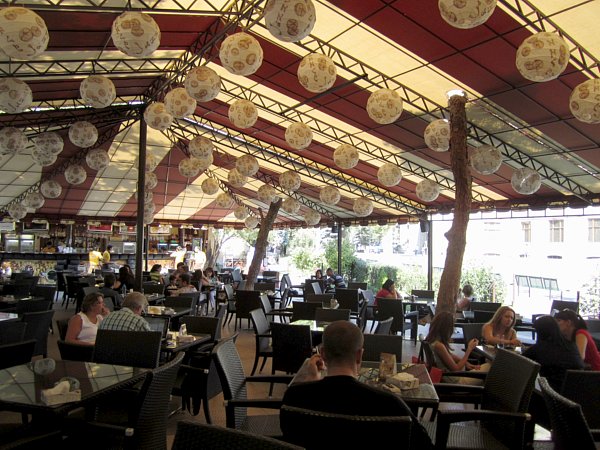 A group of people sitting at an outdoor cafe with a tent and paper lanterns overhead