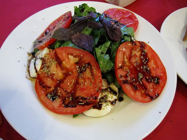 A white plate of salad with tomato and mozzarella slices with balsamic vinegar