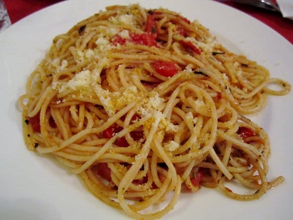 A closeup of a plate of spaghetti with tomatoes and cheese