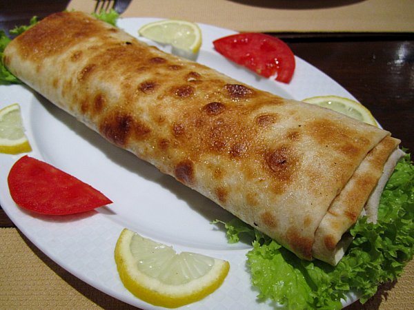 a crispy fried wrap on a white platter garnished with lemon and tomato slices